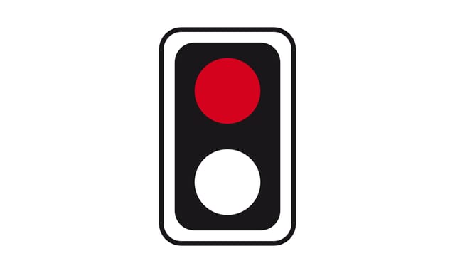Vor einem Bahnübergang steht vor einer von rechts einmündenden Straße ein rot leuchtendes Lichtzeichen ohne Andreaskreuz. Wo müssen Sie warten?